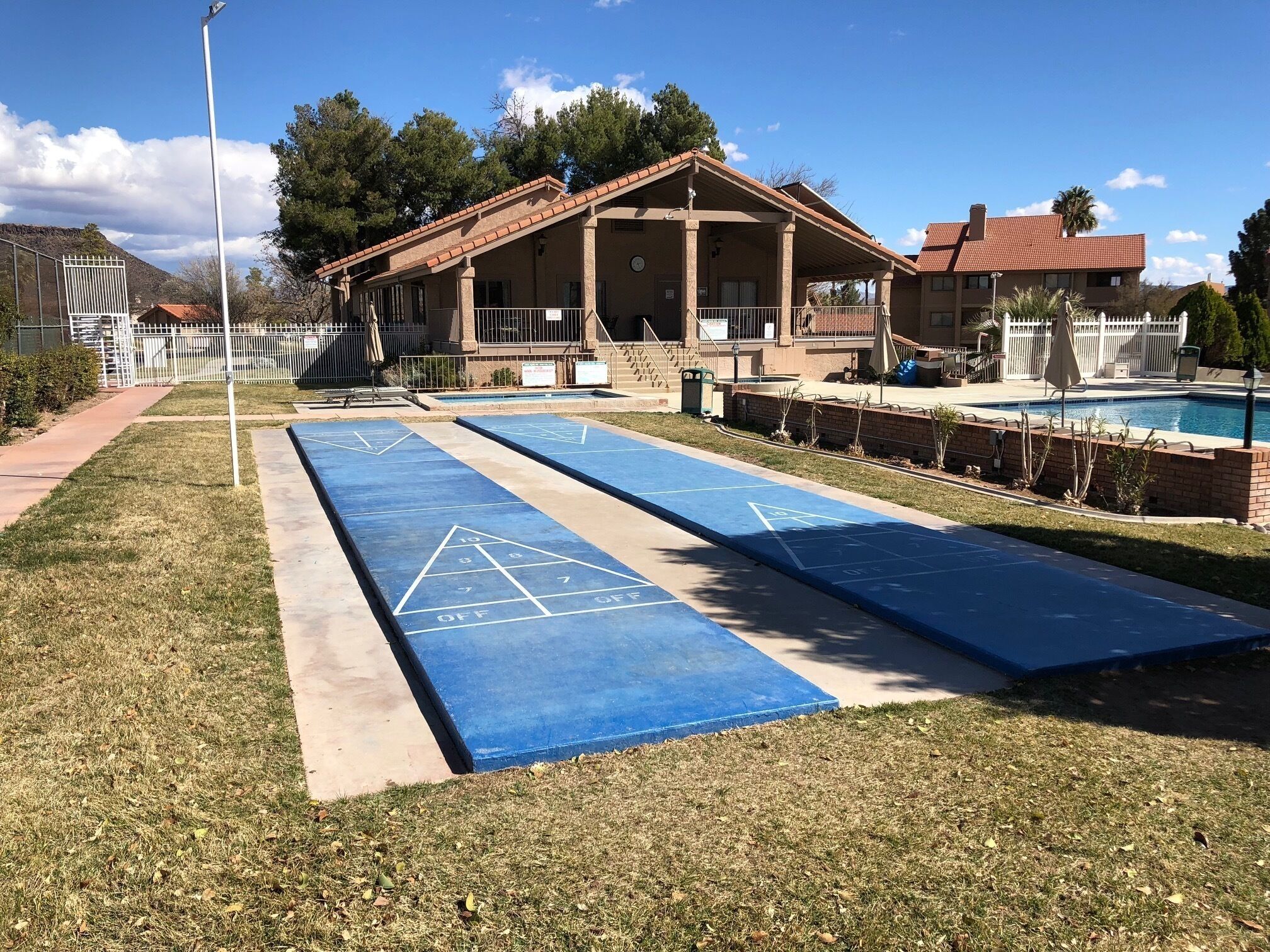 Ein Innenhof mit Shuffleboardfeld, Schwimmbecken und einem Gebäude mit Terrasse.