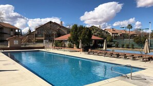 A rectangular swimming pool with a metal ladder, surrounded by lounge chairs and umbrellas, with residential buildings in the background. - Sparkling Newly Remod Condo. Near Zion's, Tuacahn, Bike Trails. Pool &Pickleball (St George)