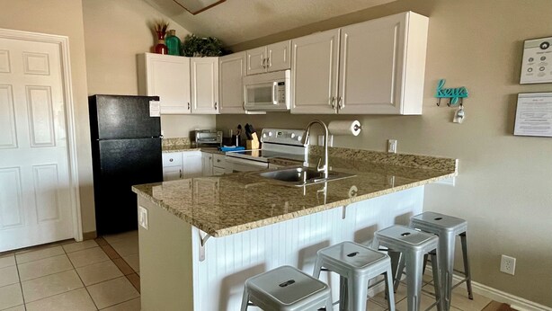 A kitchen with white cabinets, a black refrigerator, a granite countertop, and four bar stools. - Sparkling Newly Remod Condo. Near Zion's, Tuacahn, Bike Trails. Pool &Pickleball (St George)