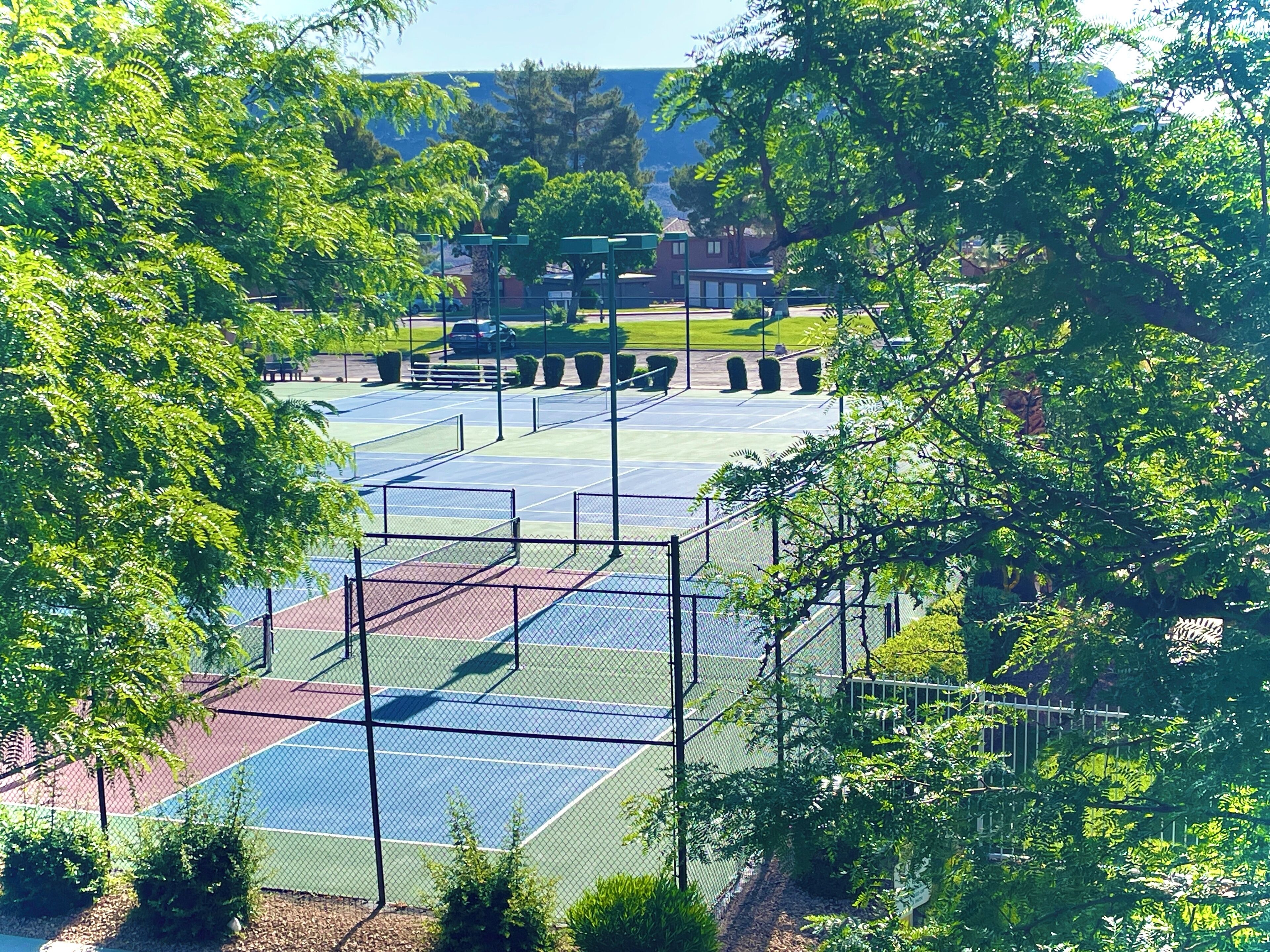 Una pista de tennis envoltada d'arbres i un edifici al fons.