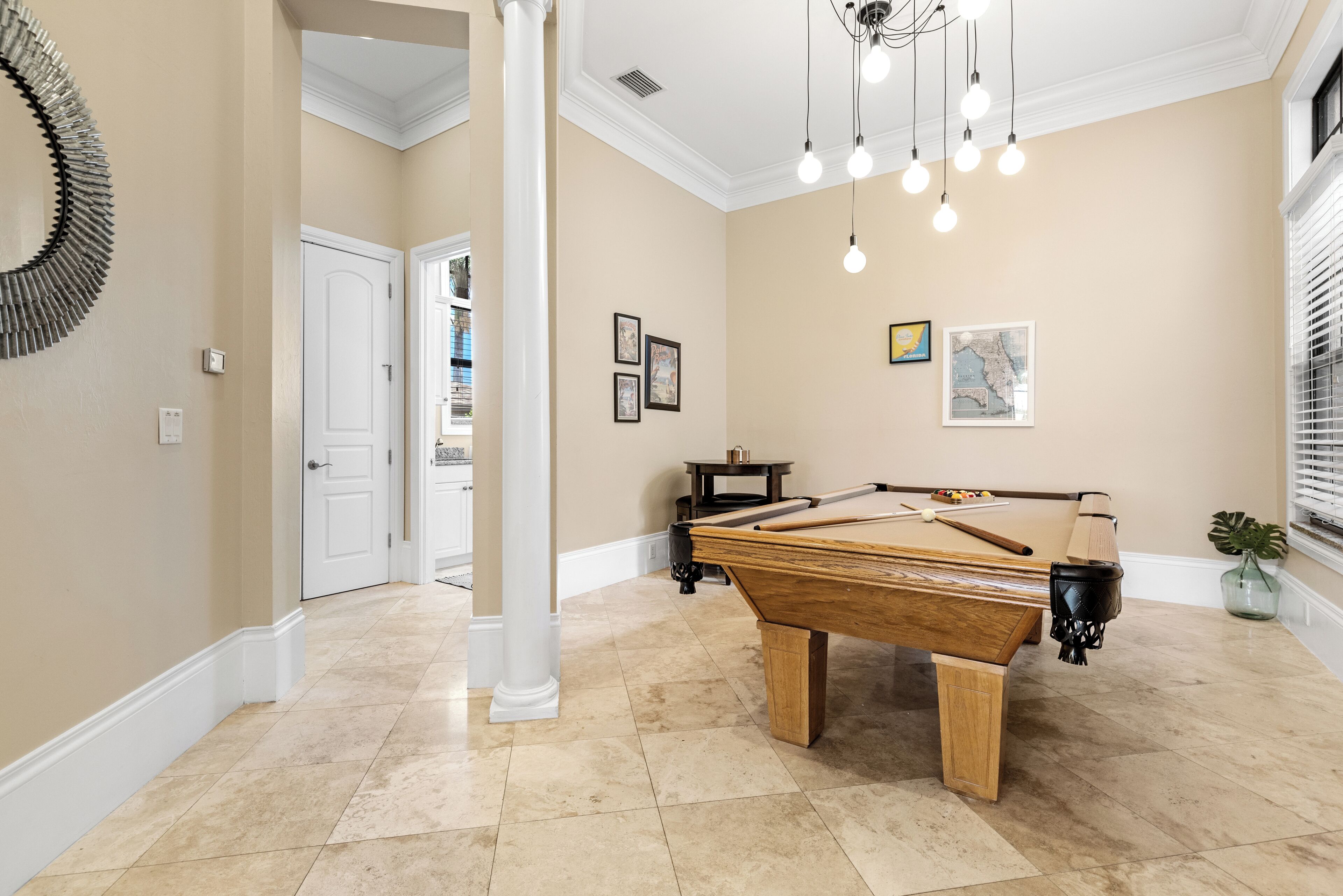 A pool table in a room with beige walls, a chandelier, and framed pictures.