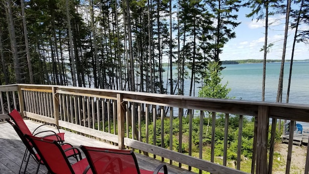 A wooden deck with red chairs overlooking a lake, surrounded by tall trees. - Large Oceanfront house in Gouldsboro, Maine near Acadia NP; Views! (Gouldsboro)