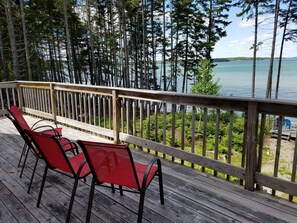 A wooden deck with red chairs overlooking a lake, surrounded by tall trees. - Large Oceanfront house in Gouldsboro, Maine near Acadia NP; Views! (Gouldsboro)