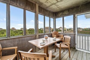 A wooden deck with a table and chairs, large windows offering a view of houses and greenery. - Ocean Views! Dog Friendly Home in Salvo w/ Hot Tub, Elevator, and Screened Porch (Salvo)