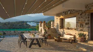 Une terrasse extérieure avec une table et des chaises en pierre, des plantes en pot et une vue sur les montagnes.