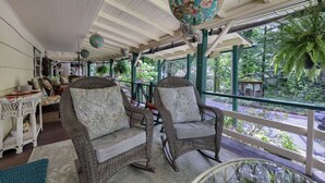 Un porche cubierto con muebles de mimbre, un globo terráqueo y vistas al verdor.