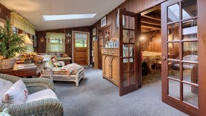 Una habitación acogedora con techo alto, un amplio armario de madera, un sofá de mimbre y una zona de comedor con mesa y sillas.