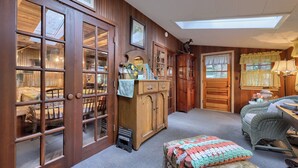 Una habitación acogedora con paredes de madera, un tragaluz, un armario de madera, muebles de mimbre y una ventana con cortinas.