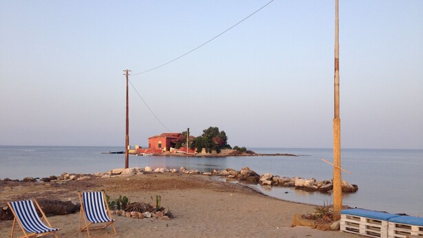 Une plage avec deux chaises de plage à rayures, un banc en bois et une petite construction surmontée d’un toit rouge.