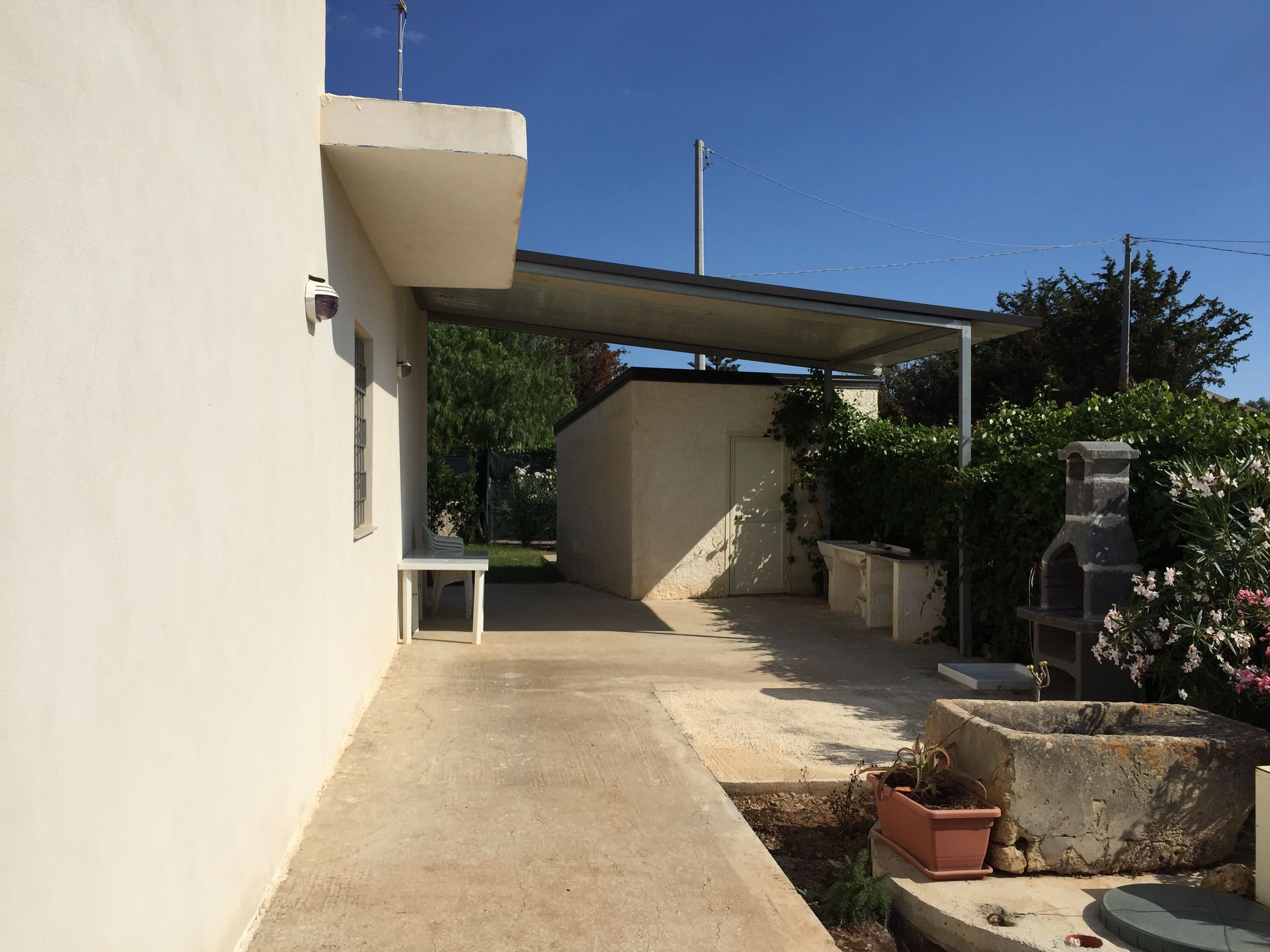 Un patio couvert avec un sol en béton, une table blanche et des plantes en pot.