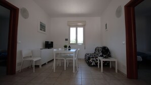 Une petite pièce bien éclairée, avec une table à manger, des chaises, un canapé et un téléviseur.