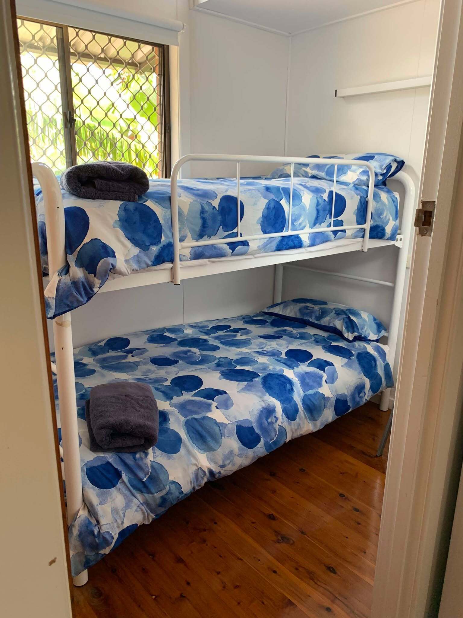 Ein Etagenbett mit blumigem, blauem Überwurf, ein Fenster mit Blick auf Grünflächen und Holzboden.