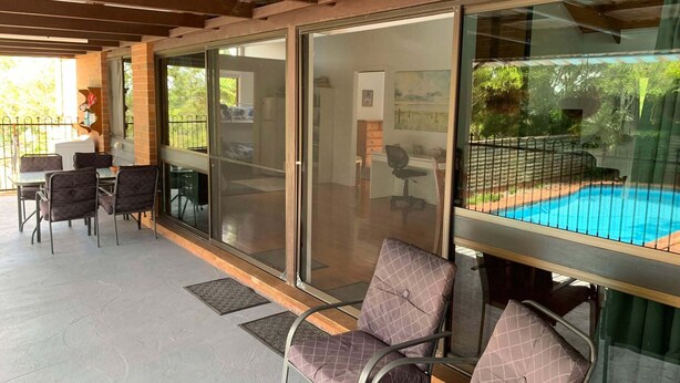 A covered patio with a pool view, sliding glass doors, and outdoor seating. - Cranley Garden Retreat with Fireplace & Pool (Cranley)