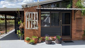 A modern house with a brick facade, a large window, and a door. There are potted plants in front of the house. - Cranley Garden Retreat with Fireplace & Pool (Cranley)