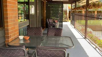Eine Terrasse im Freien mit Tisch und Stühlen, einer Ziegelwand und einem Metallzaun.