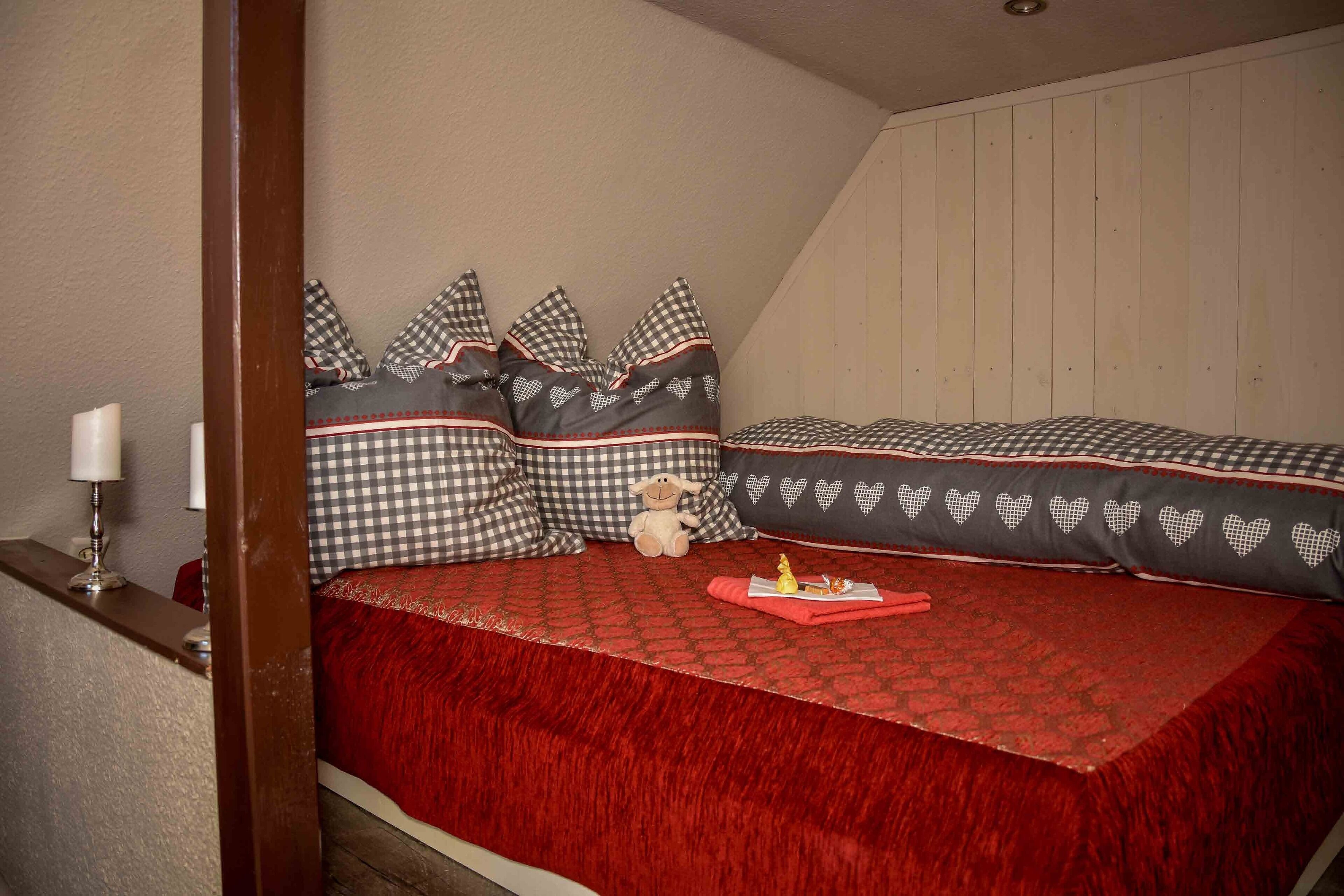 Un dormitorio con colcha roja, almohadas estampadas y un peluche pequeño.