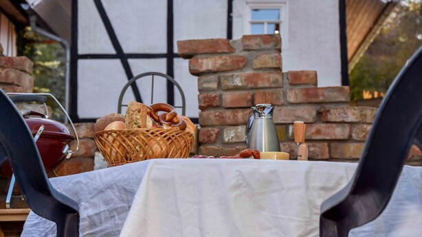 Une table dressée à l’extérieur, avec un panier de pain, une bouteille et une bouilloire.