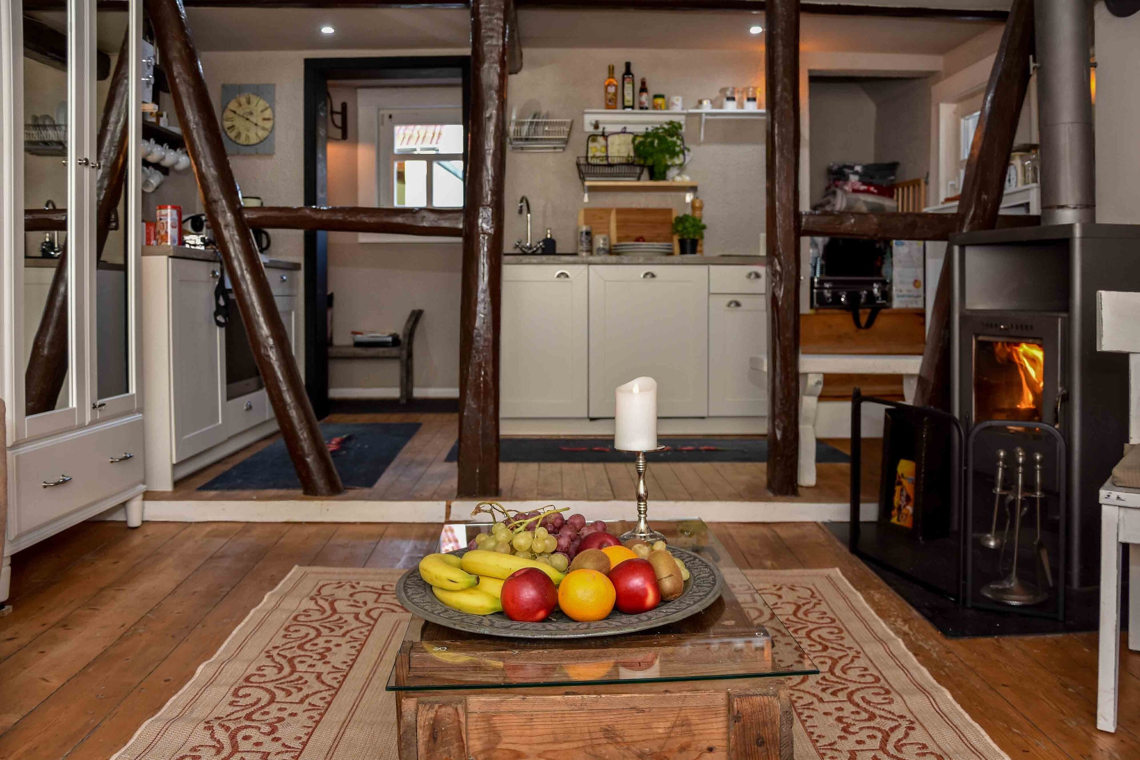 Una cocina con un frutero sobre una mesa de cristal, vigas de madera y una chimenea.