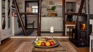 Une cuisine avec un panier de fruits posé sur une table en verre, des poutres en bois et une cheminée.