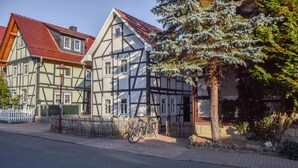 Une maison traditionnelle à colombages, avec un toit recouvert de tuiles rouges, une clôture blanche et des vélos garés devant.