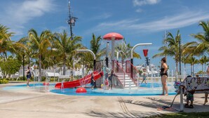 Un parque acuático con un tobogán rojo, chorros de agua y palmeras.