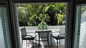 Un patio con una mesa, dos sillas, una puerta de vidrio y vistas a plantas.