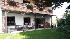 A covered outdoor area with a patio table and chairs, a stack of firewood, and a garden with a wooden fence. - 80 m², family-friendly, barrier-free apartment, overlooking the golf course (Sundern (Sauerland))