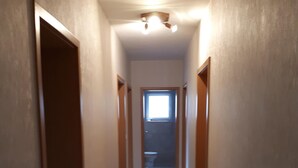A narrow, well-lit hallway with wooden doors on either side, leading to a room with a window at the end. - 80 m², family-friendly, barrier-free apartment, overlooking the golf course (Sundern (Sauerland))