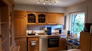 A kitchen with wooden cabinets, a stainless steel dishwasher, an oven, and a window with a view of greenery. - 80 m², family-friendly, barrier-free apartment, overlooking the golf course (Sundern (Sauerland))