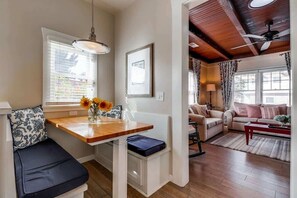 A cozy living room with a wooden dining table, a sofa, and a ceiling fan.