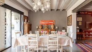 Comedor con una mesa grande dispuesta para seis personas, rodeado de sillas blancas.