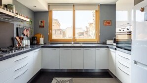 Una cocina moderna con armarios blancos, encimera negra, estufa y ventana con vista a edificios.