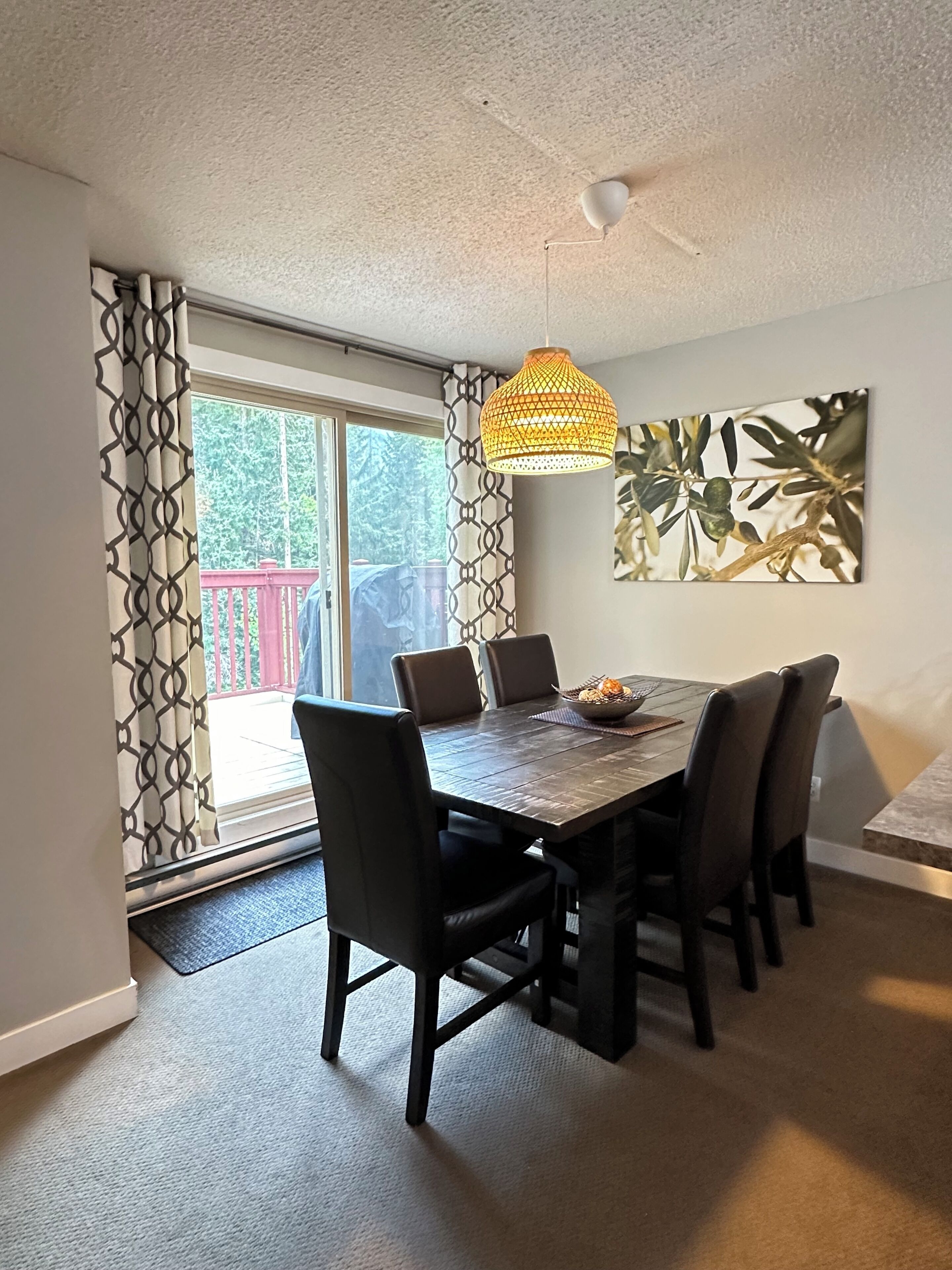 A dining area with a wooden table, black chairs, a woven pendant light, and a large abstract painting on the wall.