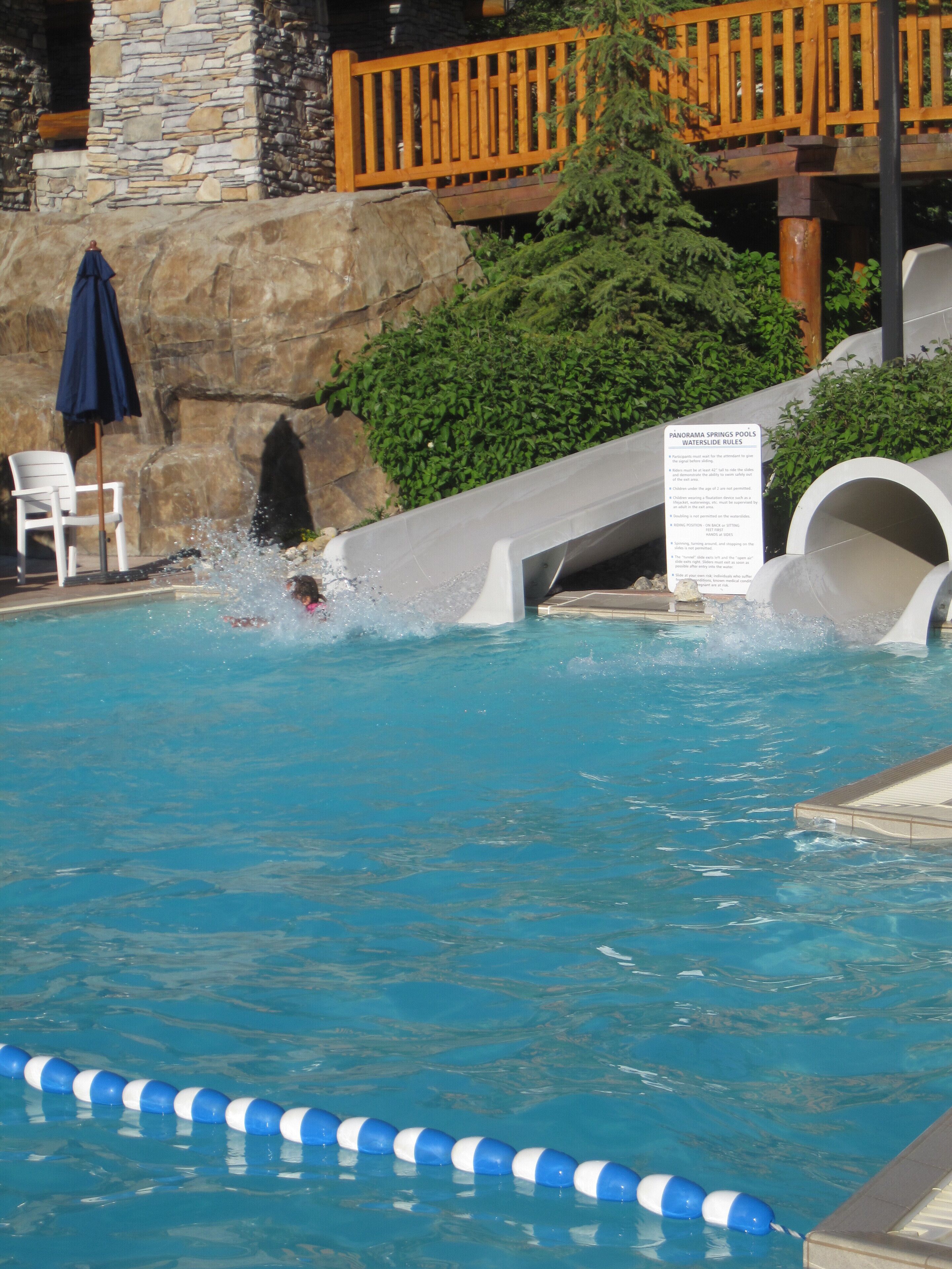 Une piscine avec un toboggan, un mur en pierre et une terrasse en bois.