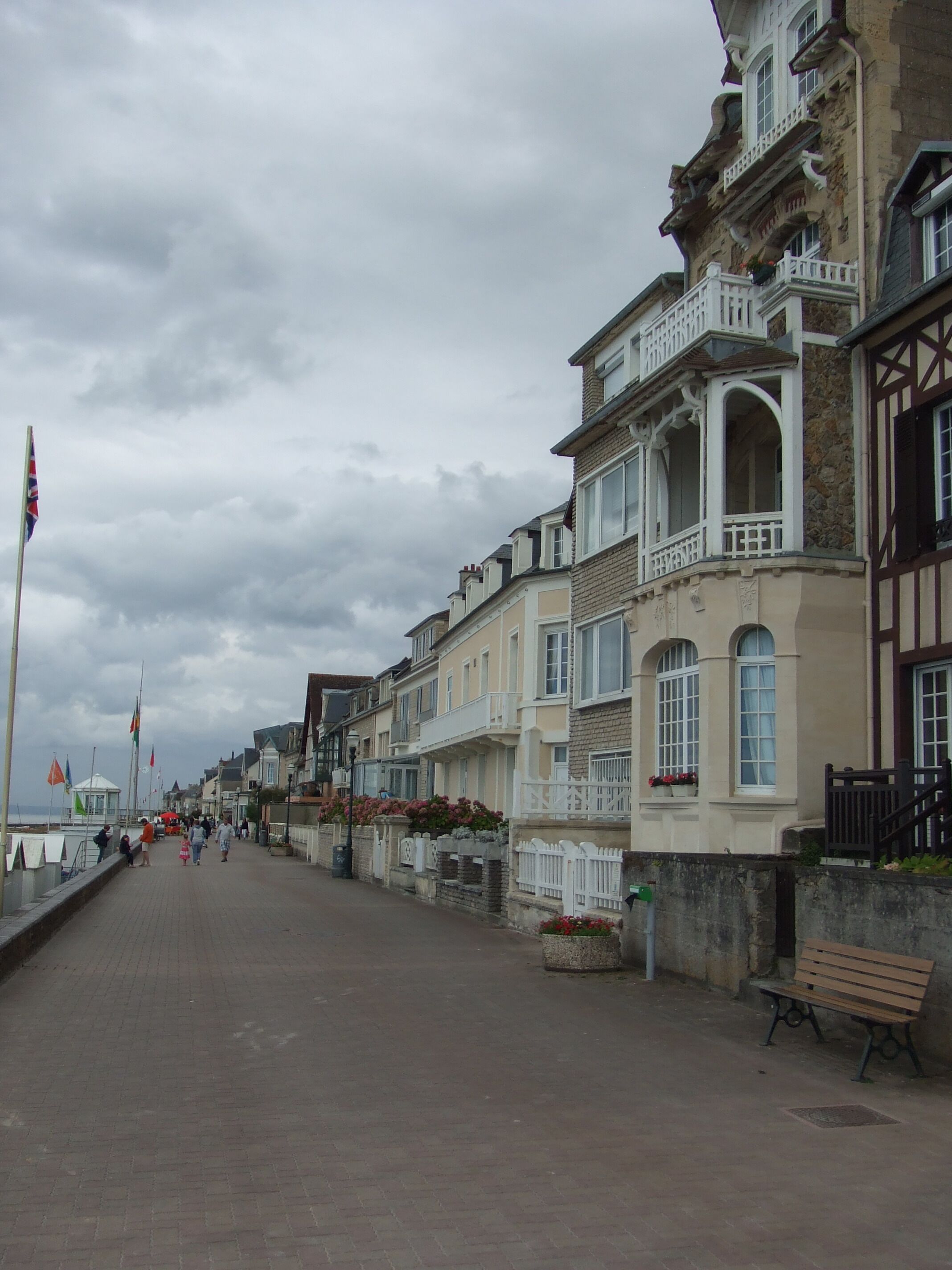 Un paseo marítimo con edificios tradicionales, un banco y banderas.