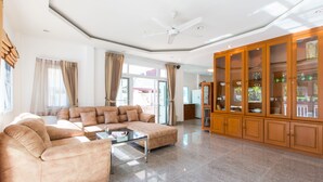 Un salón espacioso con un sofá modular grande, una mesa de centro de vidrio y un aparador de madera con puertas de cristal.