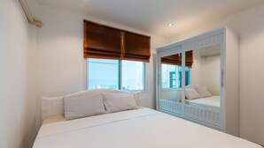 Un dormitorio con una cama grande, una ventana con persianas marrones, un radiador blanco y un espejo con marco blanco.