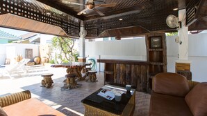 Un área de estar al aire libre con mobiliario de mimbre, una mesa de madera y un ventilador de techo.