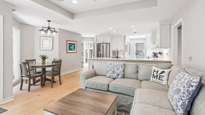 A modern living room with a gray sofa, wooden coffee table, and a dining area with a table and chairs.