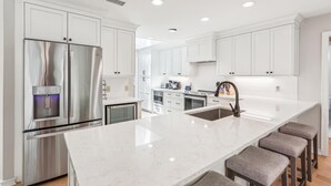 A modern kitchen with white cabinetry, stainless steel appliances, a marble countertop, and bar stools.
