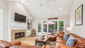 A spacious living room with leather sofas, a fireplace, a television, and a dining area with outdoor views.