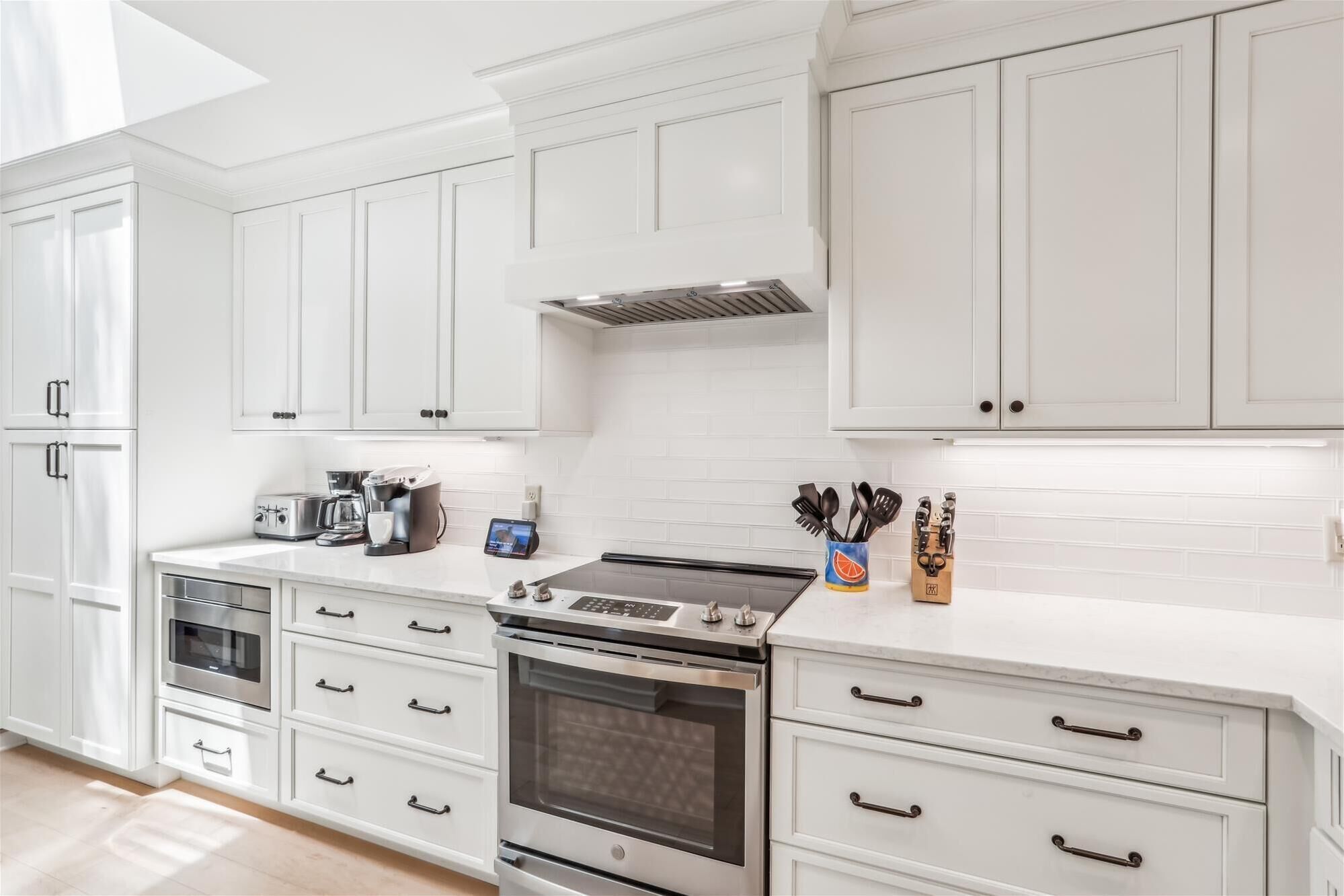 A modern kitchen with white cabinetry, stainless steel appliances, and a built-in oven.