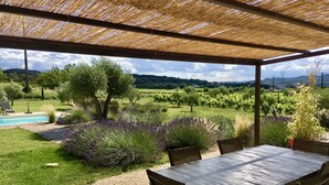 An outdoor patio with a table and chairs, a pool, and a view of a vineyard and hills. - Holiday home for 8 people (Vénéjan)