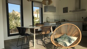 A modern kitchen with large windows, a dining area with wicker chairs, and a view of trees and buildings outside. - Holiday home for 8 people (Vénéjan)