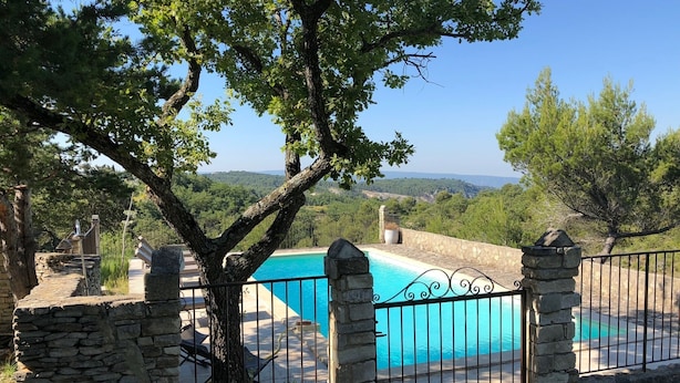 Una piscina privada con muros de piedra y valla metálica, rodeada de árboles y una vista panorámica.