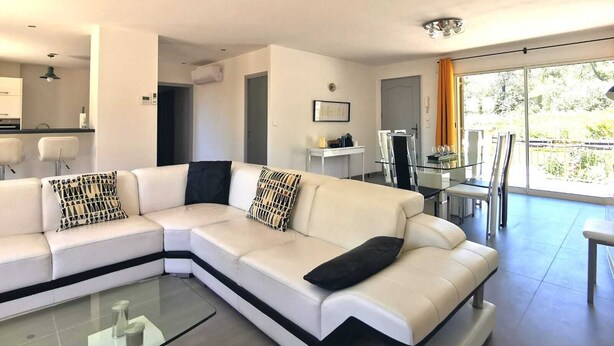 Una sala moderna con un sofá modular, una mesa de centro de vidrio y una zona de comedor con una mesa y sillas de vidrio.