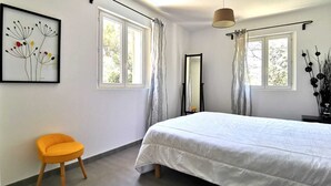 Un dormitorio con cama, una silla, un espejo y obras de arte en la pared.