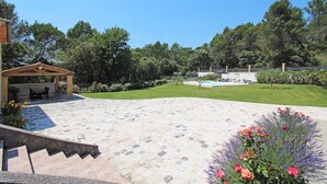 Un patio con piso de piedra, una pérgola con mobiliario y una piscina al fondo.