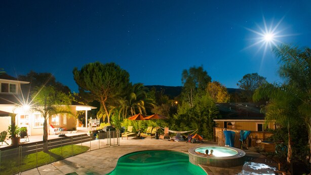 A swimming pool with a hot tub, lounge chairs, and umbrellas.