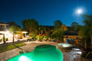 Una piscina con hidromasaje, sillas de descanso y sombrillas.